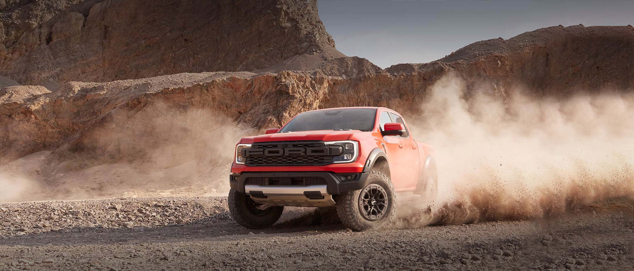 Blue Ford Ranger Raptor driving through a countryside, front three quarter view