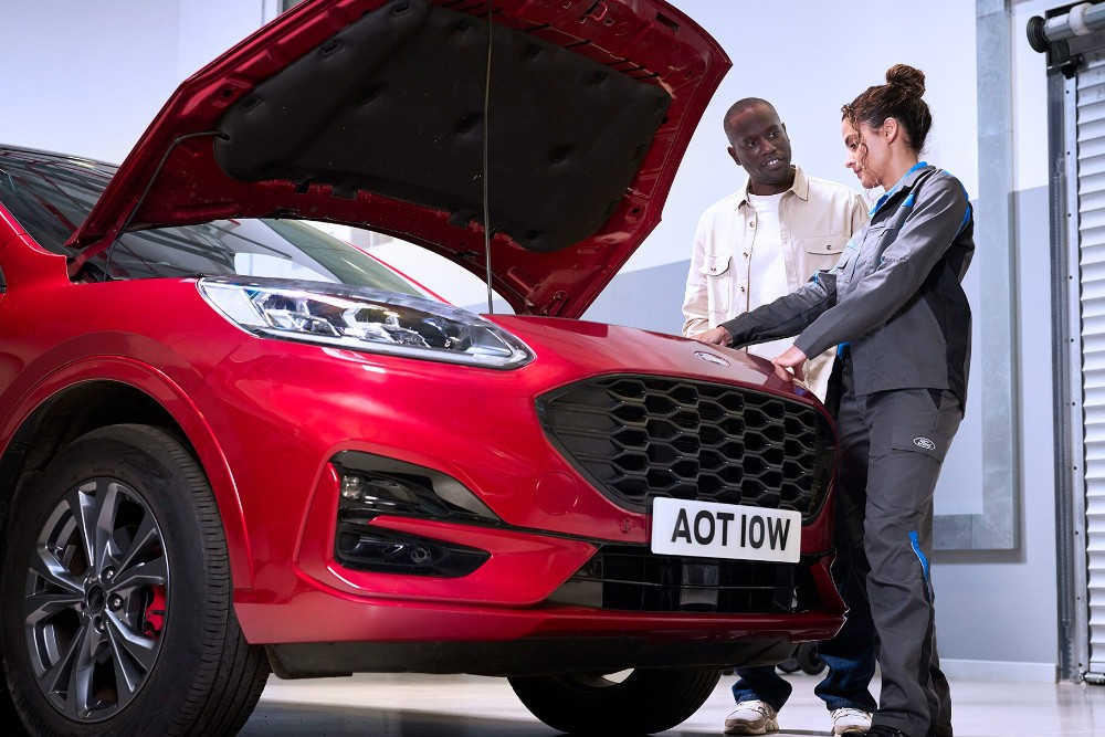 Ford Kuga vermelho com capô aberto, um técnico e uma pessoa inspecionando o compartimento do motor