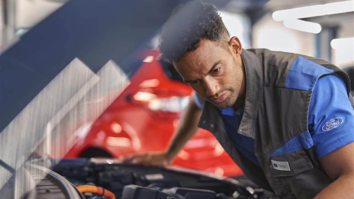 Um técnico com uniforme da Ford a trabalhar no motor de um veículo Ford vermelho.