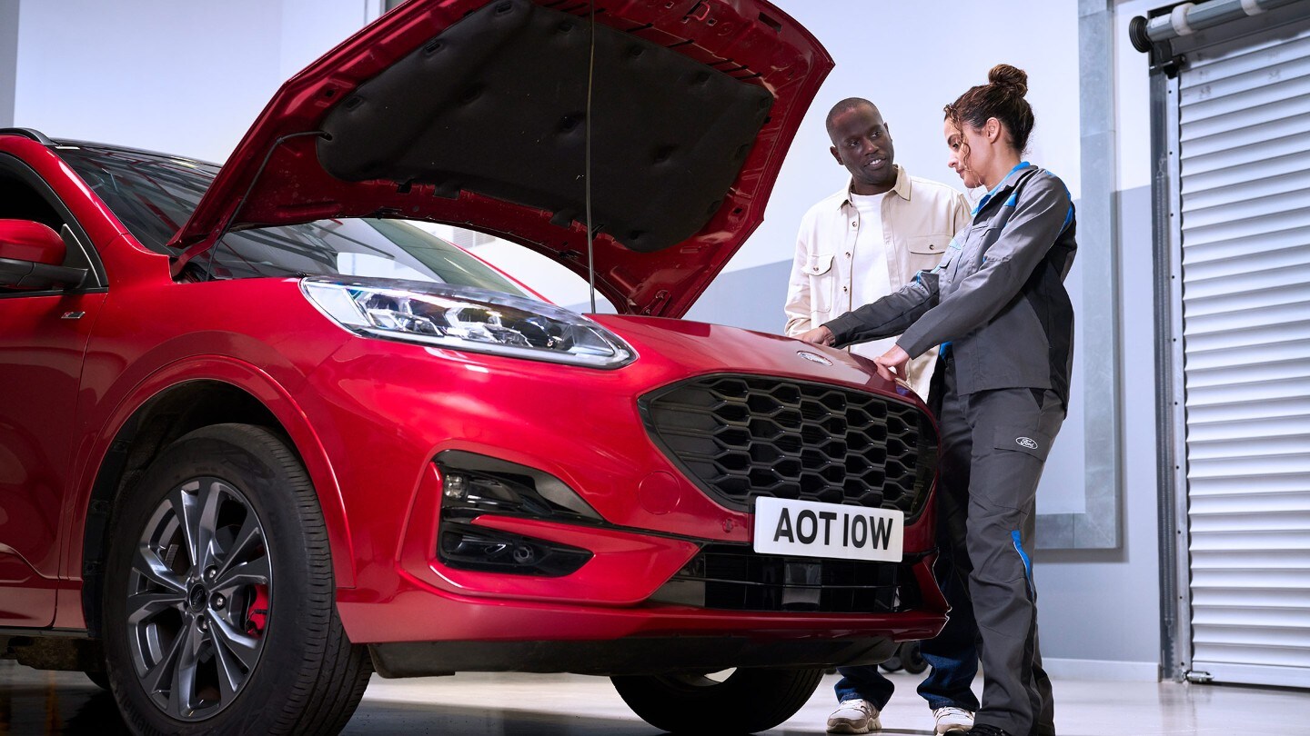 Ford Kuga vermelho com capô aberto, um técnico e uma pessoa inspecionando o compartimento do motor