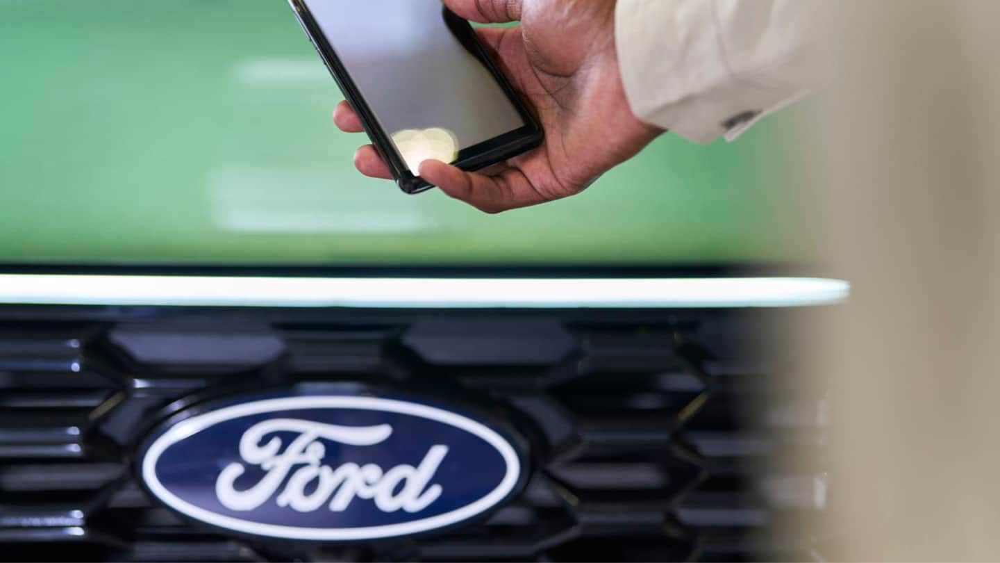 Pessoa a segurar um smartphone ao lado de um Ford verde