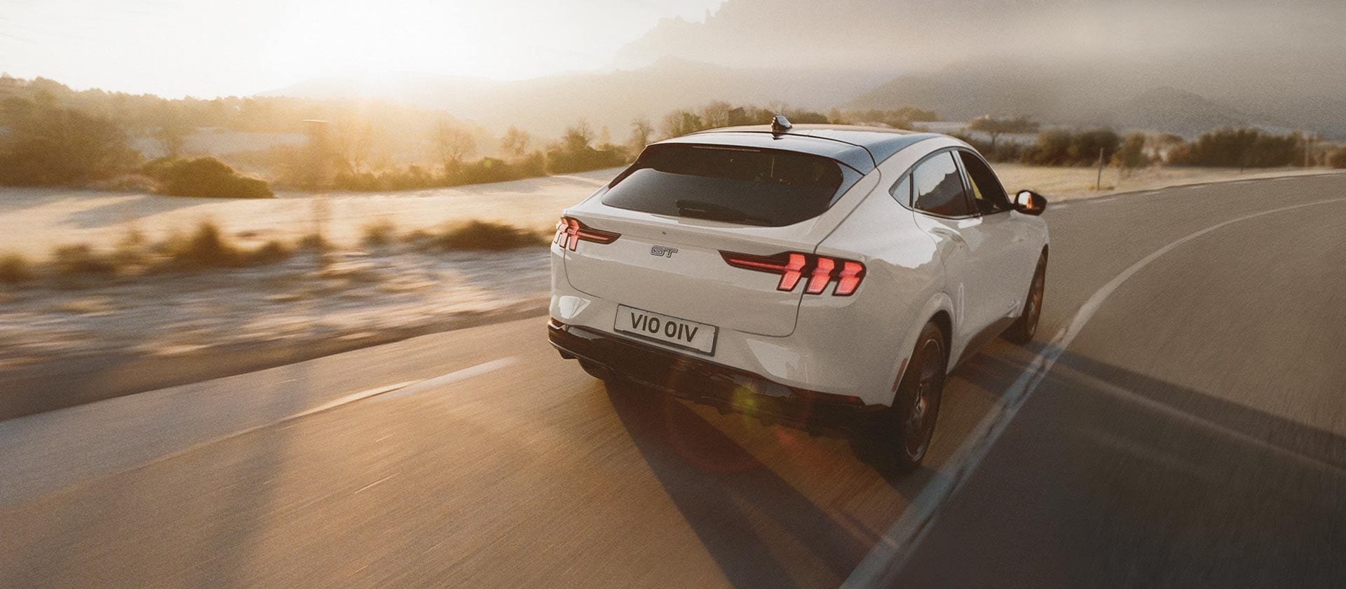 Um veículo elétrico Ford Mustang Mach-E prateado dirigindo em uma longa estrada aberta.