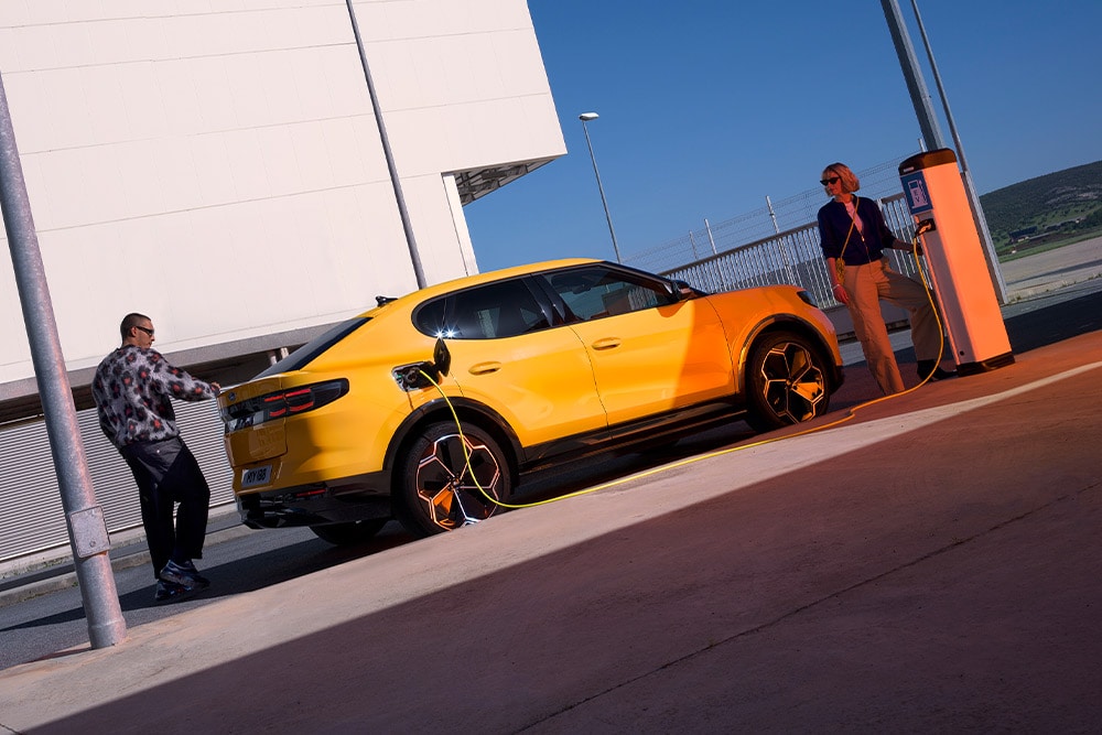 Pessoas carregando um Ford Capri EV amarelo em uma estação de carregamento pública.