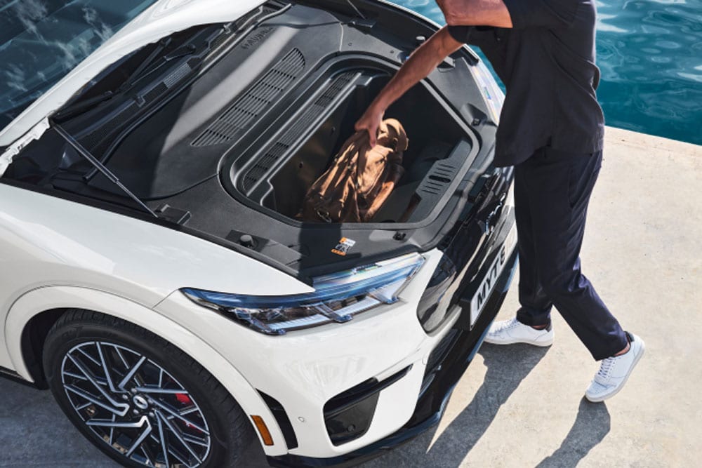 Uma pessoa colocando uma bolsa de retenção no frunk de um carro elétrico Ford Mustang Mach-E branco.
