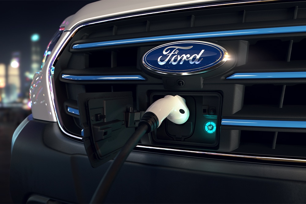 Close-up de um ponto de carregamento de van Ford E-Transit e emblema oval azul da Ford na grade frontal.