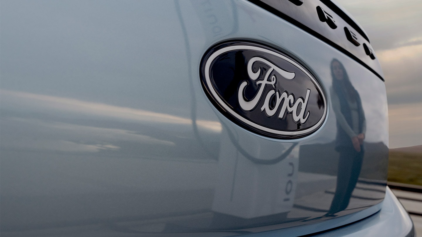 Logótipo da Ford num Ford Explorer elétrico azul com uma estação de carregamento pública refletida no automóvel.