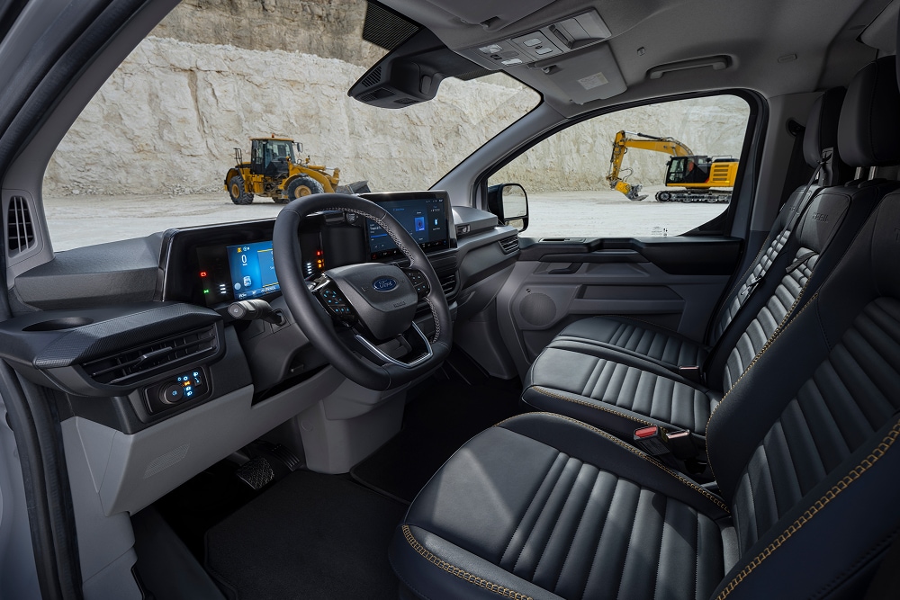 Interior de um furgão elétrico Ford E-Transit Custom, que mostra os bancos e o volante, estacionado numa pedreira.