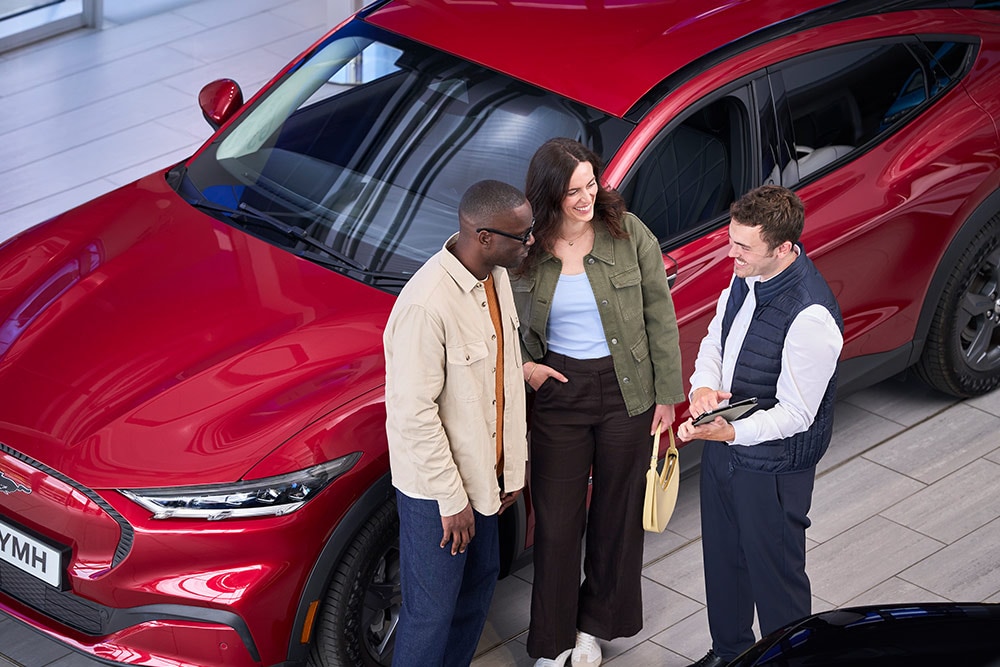 Um casal e um vendedor discutem um Ford Mustang Mach-E vermelho num stand.