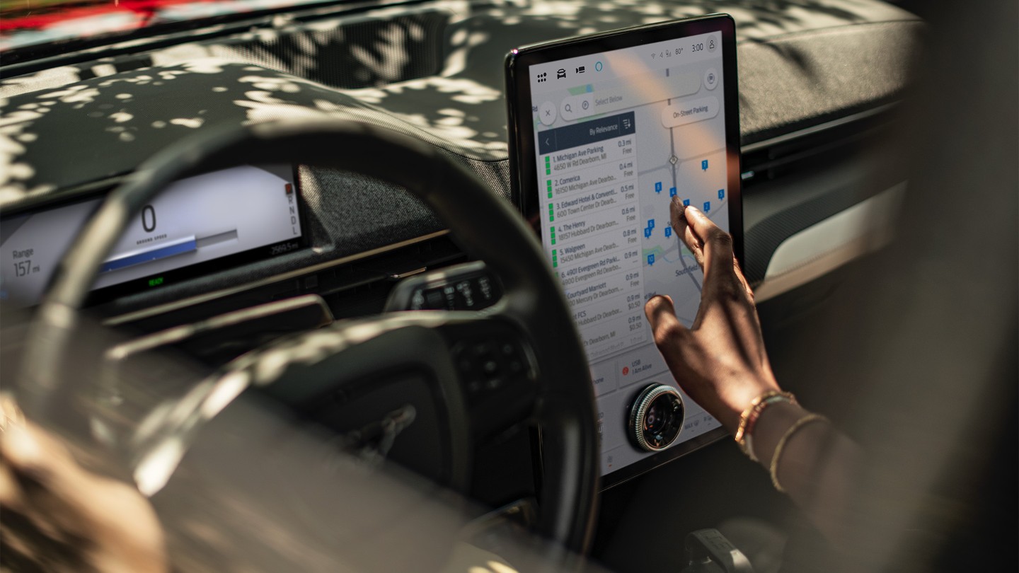 Grande plano de uma mulher num Ford Mustang Mach-E a interagir com o grande ecrã táctil do SYNC.