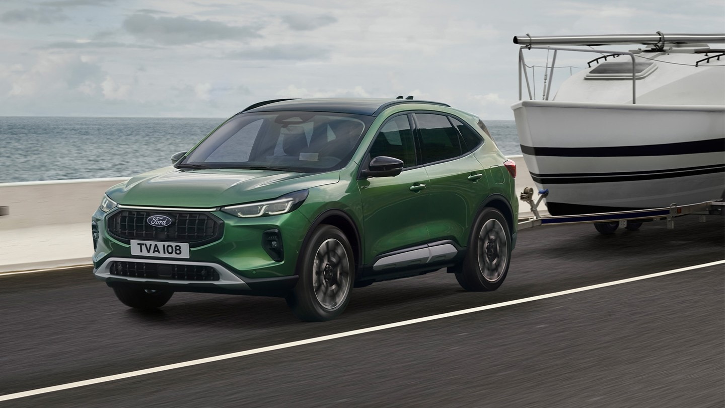 Ford Kuga verde a rebocar um pequeno barco ao longo de uma estrada costeira.