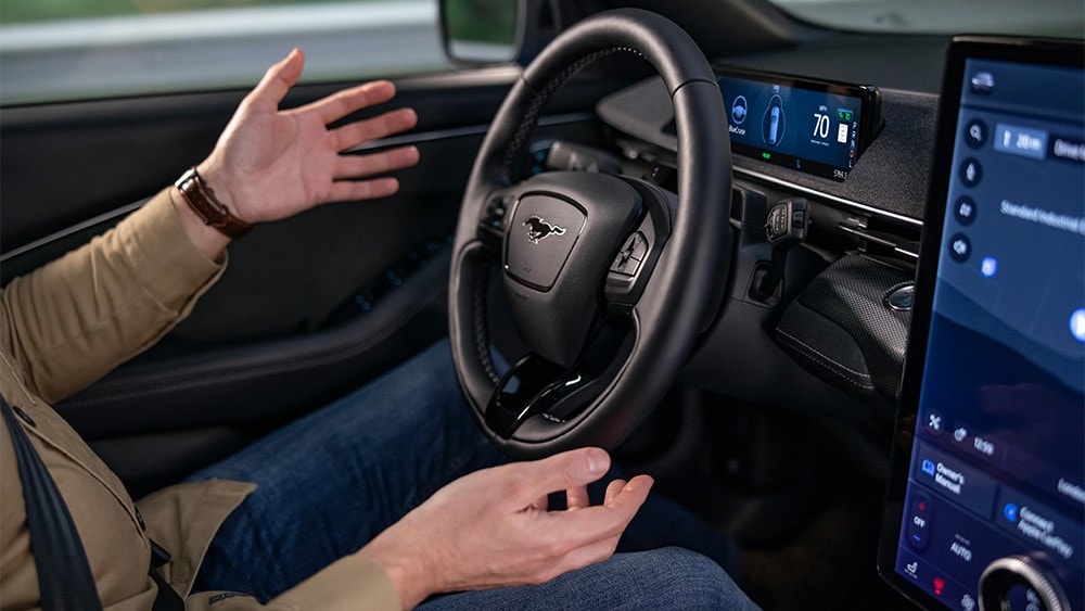 Homem sentado no Ford Mustang Mach-E com as mãos afastadas do volante, a mostrar a tecnologia BlueCruise.