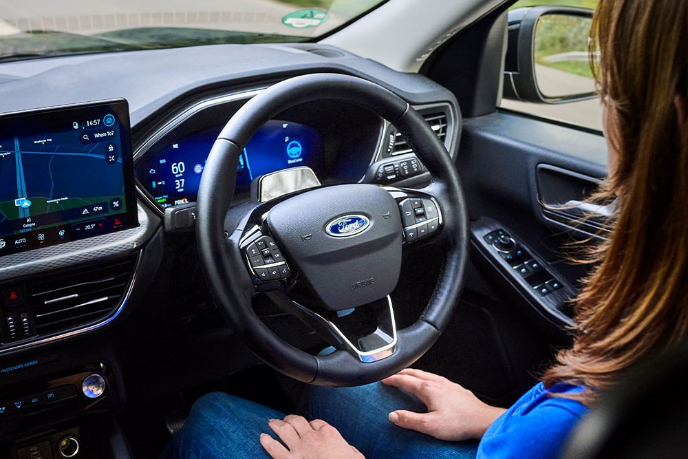 Mulher no banco do condutor de um Kuga equipado com Ford BlueCruise, com as mãos fora do volante.