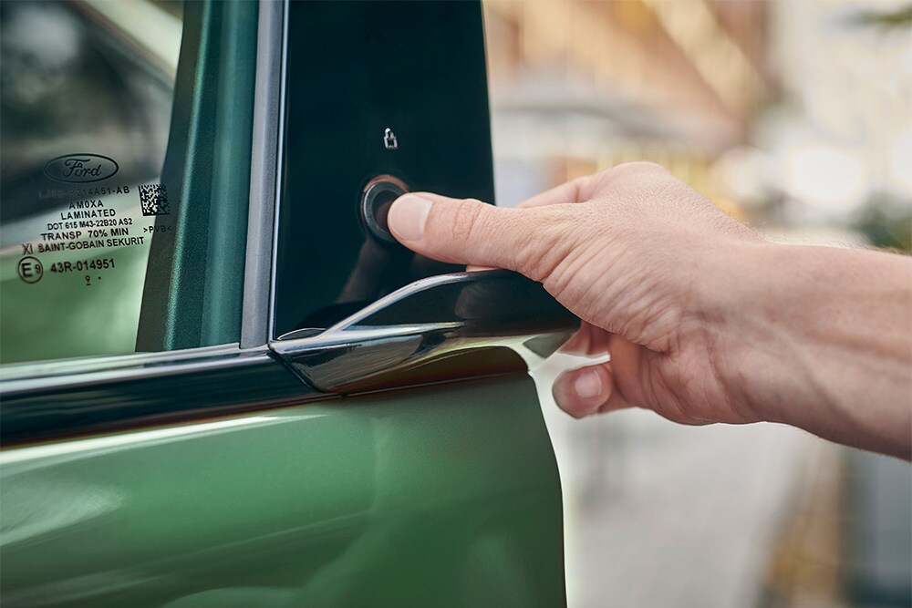 Grande plano de uma mão a operar o sistema E-LATCH ao premir um botão na porta de um Ford Mustang Mach-E verde.