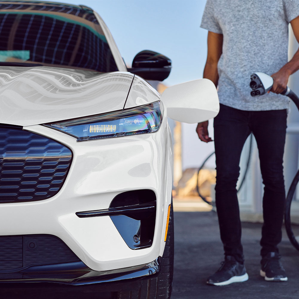 Pessoa a carregar um Ford Mustang Mach-E branco com um cabo de carregamento EV.