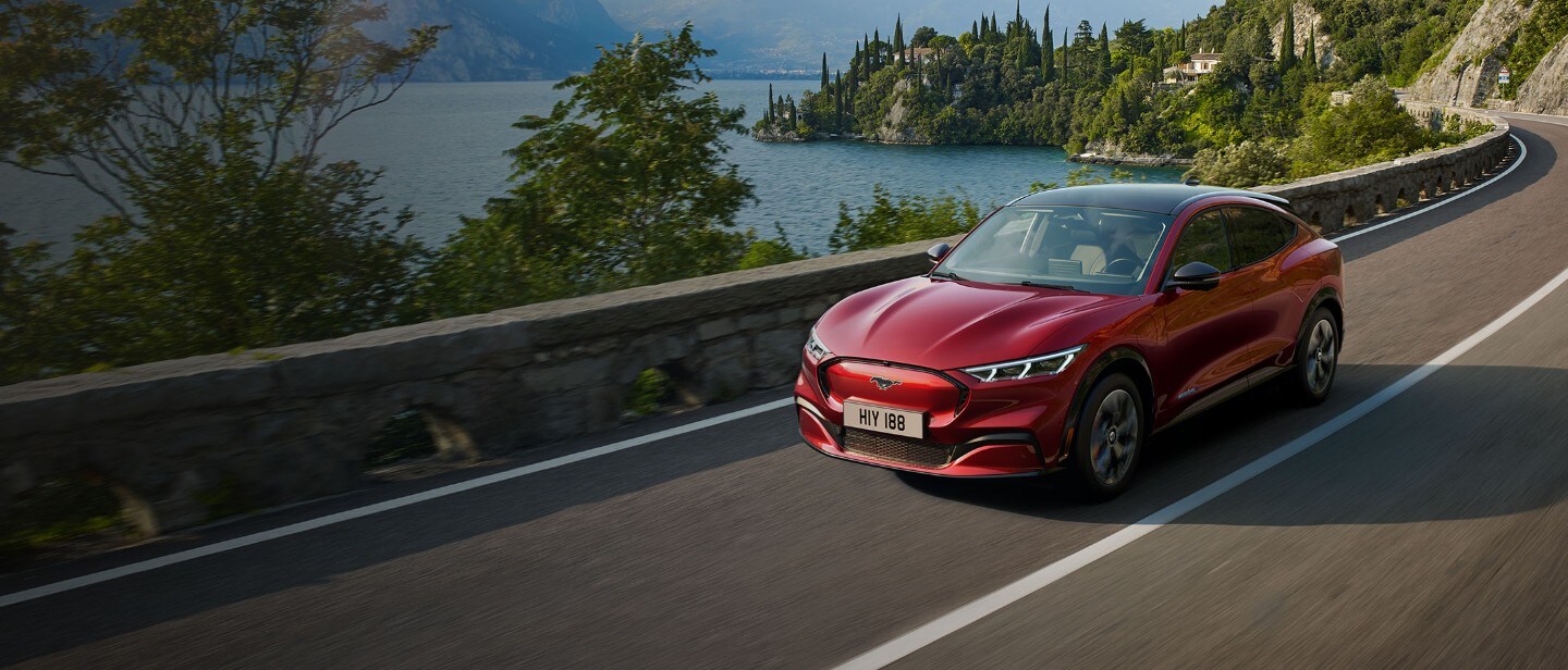Red all-electric Ford Mach-E driving past the mountain lake Red all-electric Ford Mach-E driving past the mountain lake