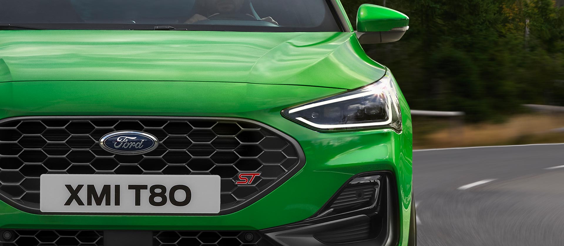Vista frontal do Ford Focus ST verde médio, mostrando a grelha em favo de mel e o emblema ST.