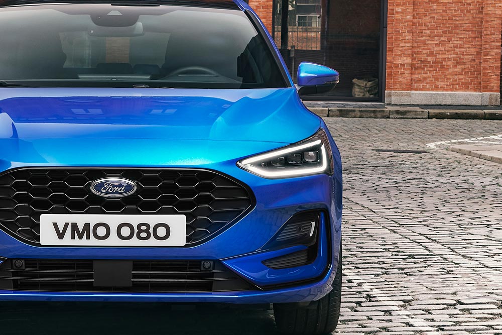 Vista frontal de um Ford Focus azul, com destaque para os faróis e grade.