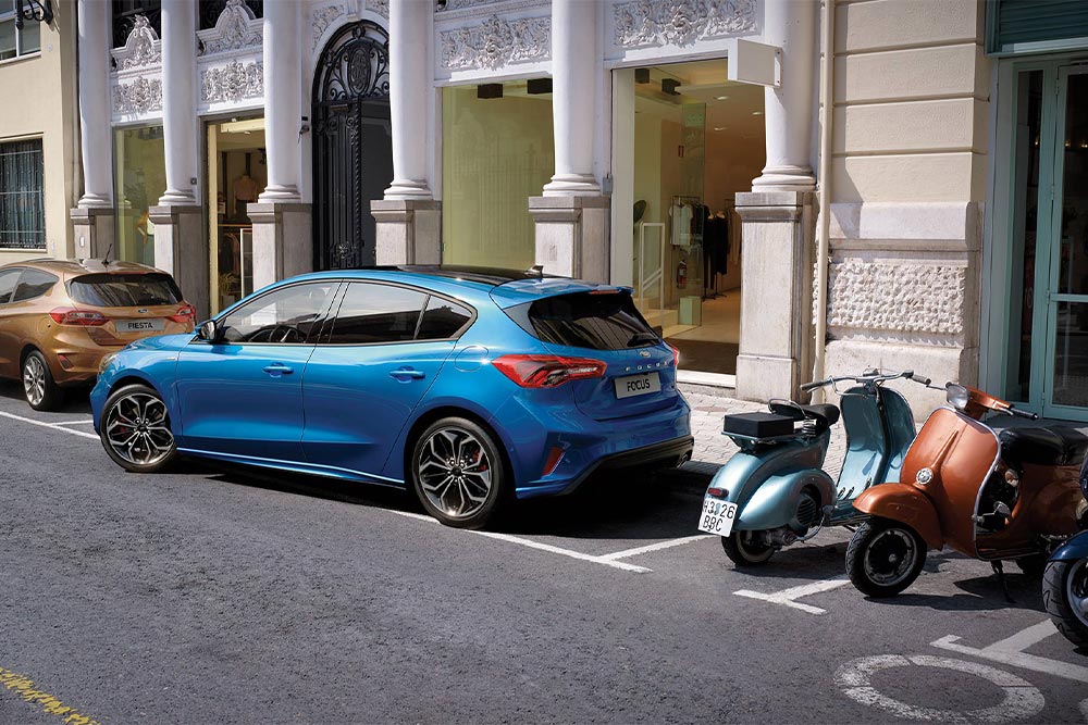 Um Ford Focus azul a manobrar num espaço de estacionamento urbano utilizando a funcionalidade Ative Park Assist.