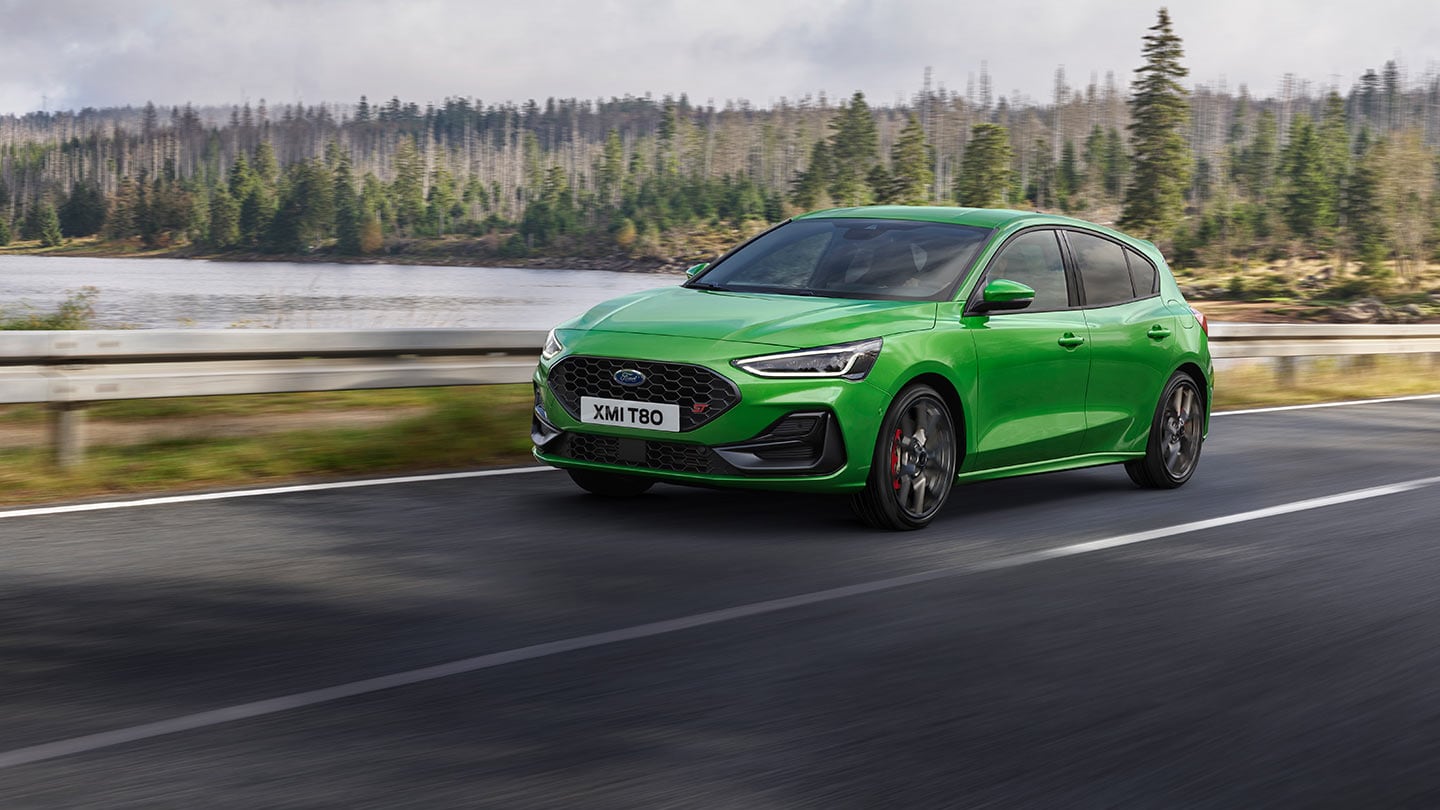 Um Ford Focus ST em Mean Green dirigindo em uma estrada com árvores ao fundo.