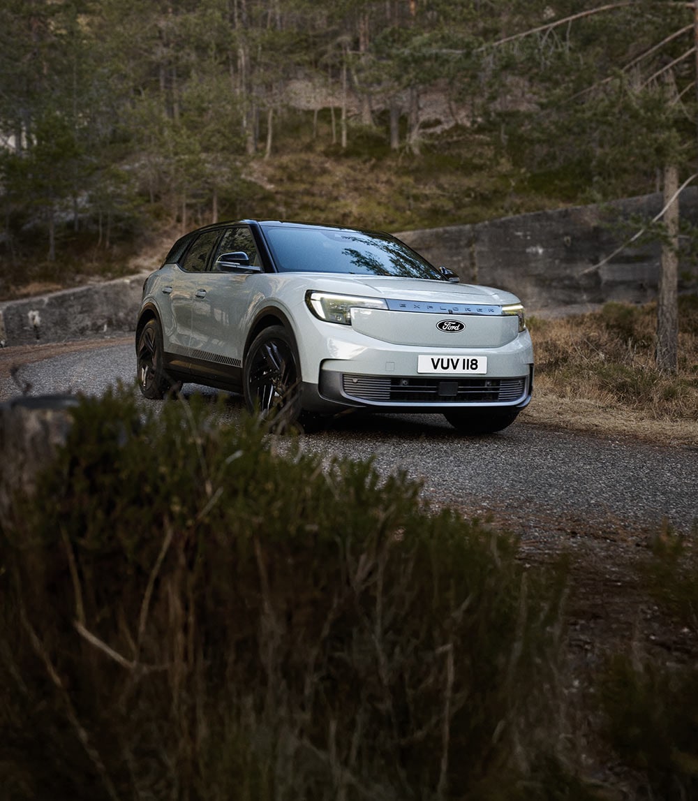 Ford Explorer prateado a percorrer uma estrada montanhosa sinuosa. 