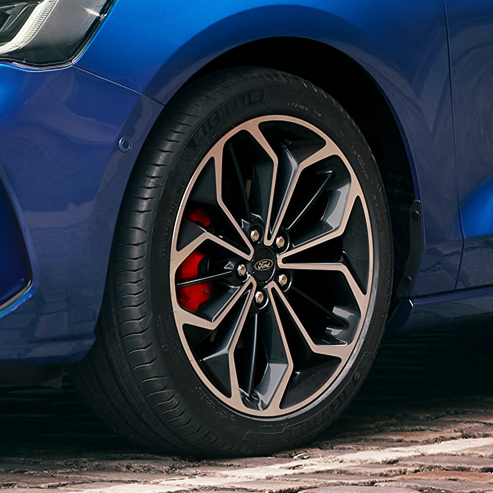 Close-up das jantes de liga leve cinzentas com pinças de travão vermelhas num Ford Focus azul.
