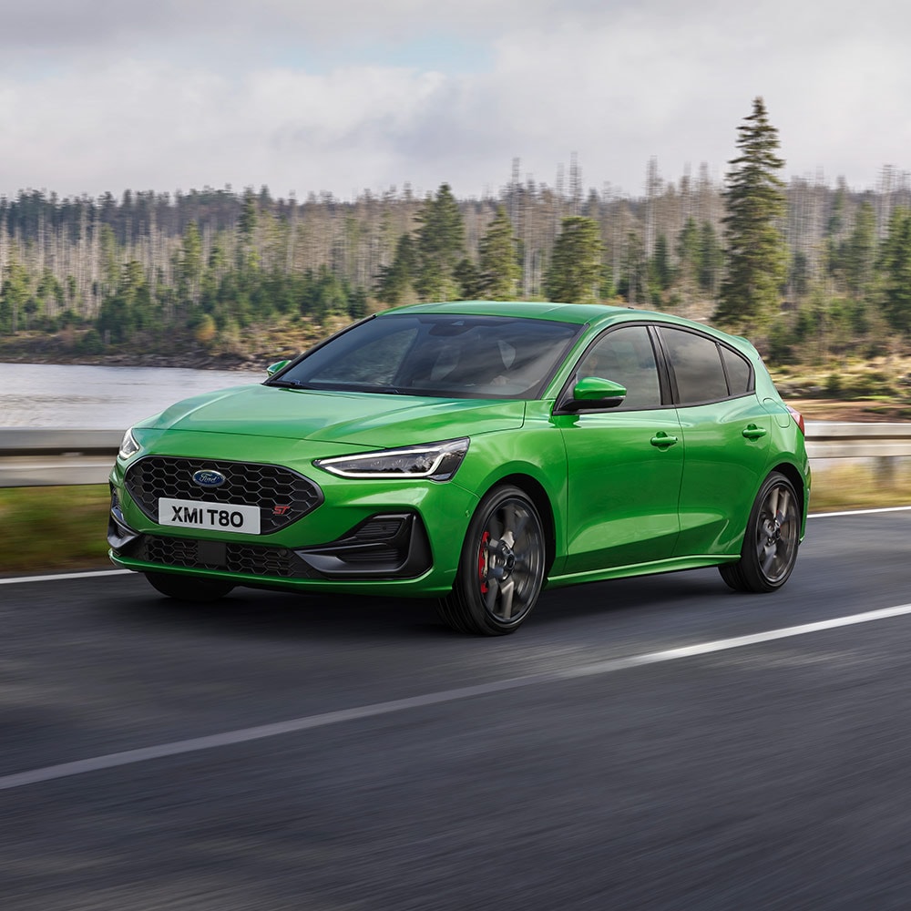 Um Ford Focus ST verde médio dirigindo em uma estrada sinuosa cercada por árvores.