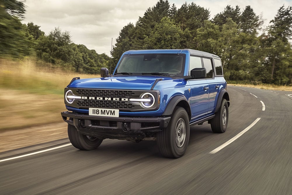 Vista da parte da frente do novo Ford Bronco em azul a percorrer uma estrada campestre.