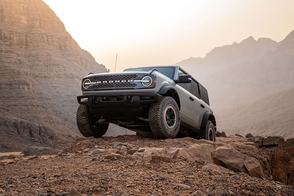 Ford Bronco cinzento estacionado no topo de um caminho rochoso num cenário de montanha.