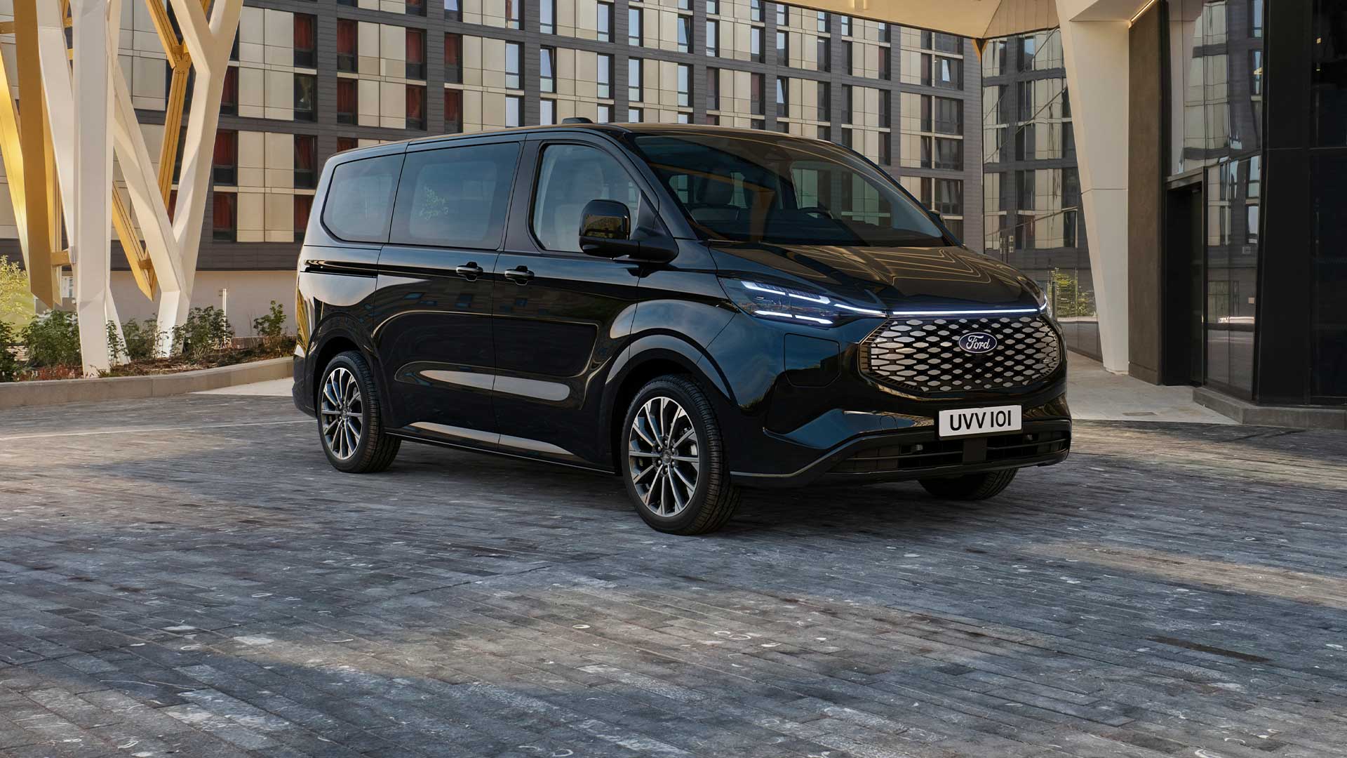 Ford E-Tourneo Custom preto estacionado em frente a um edifício moderno.