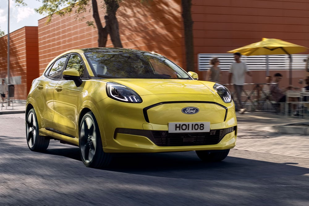 Vista frontal de um Ford Puma Gen-E® elétrico amarelo a circular numa estrada urbana.