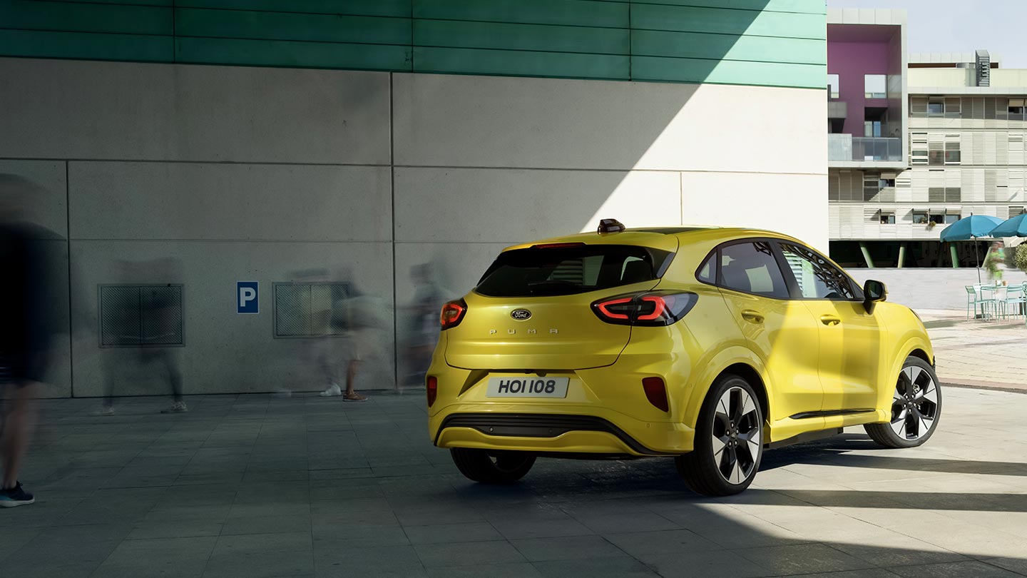 O ângulo traseiro de um Ford Puma Gen-E® elétrico amarelo estacionado debaixo de uma ponte.