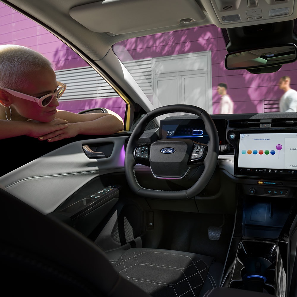 O interior do Ford Puma Gen-E® elétrico, com uma pessoa a olhar para o grande ecrã de infoentretenimento através da janela.