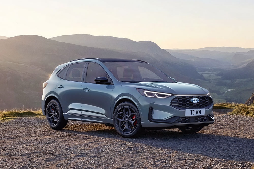 Um Ford Kuga cinzento estacionado numa estrada de montanha de gravilha ao pôr do sol.