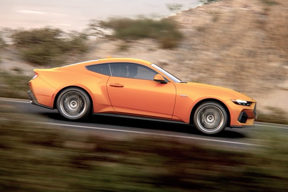 Vista lateral do Ford Mustang GT Fastback em Orange Fury a percorrer uma estrada