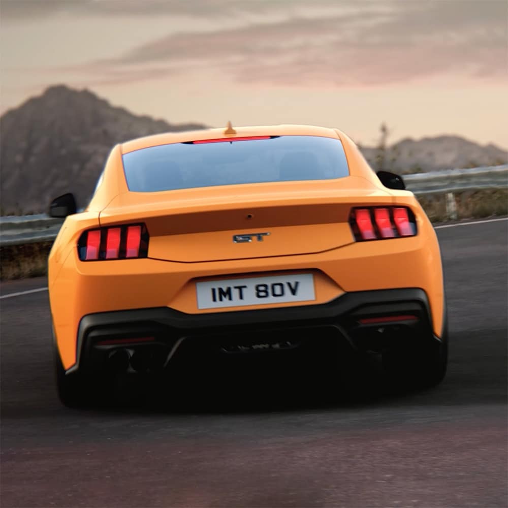 A traseira de um Ford Mustang GT Fastback em Orange Fury a fazer uma curva apertada numa estrada rural