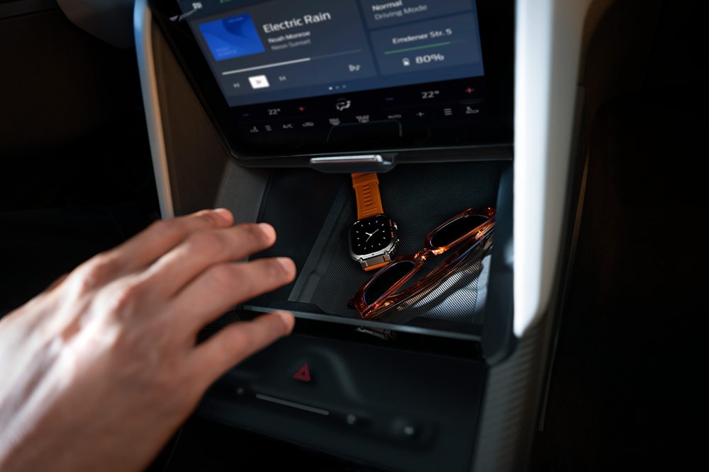 Mão estendida em direção ao compartimento My Private Locker no Ford Capri®, mostrando um relógio e um par de óculos de sol no interior.