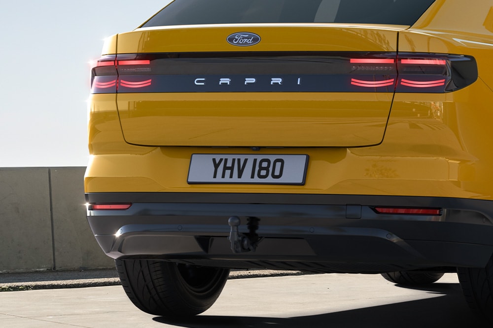 Vista traseira de um Ford Capri® em amarelo a percorrer uma estrada urbana.