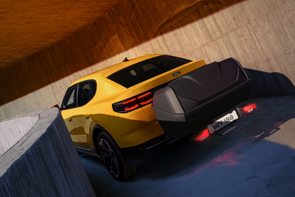 Ford Capri amarelo num parque de estacionamento moderno, com mala bagageira instalada num atrelado acoplado à traseira.