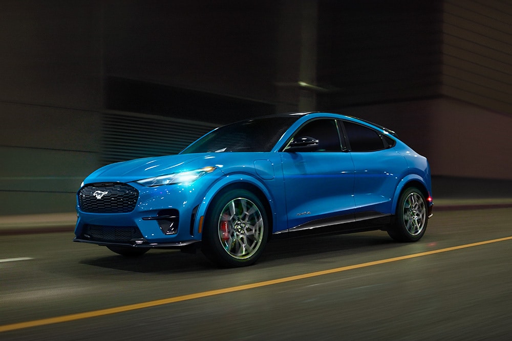 Um carro desportivo elétrico azul Ford Mustang Mach-E GT, percorrendo uma estrada aberta.