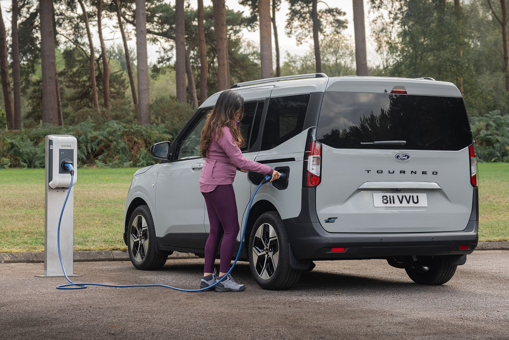 Uma pessoa liga um Ford E-Tourneo Courier cinzento a um posto de carregamento exterior.