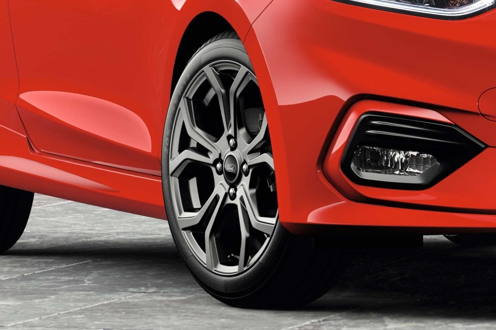 Grande plano da jante em liga leve e do para-choques dianteiro de um Ford vermelho.