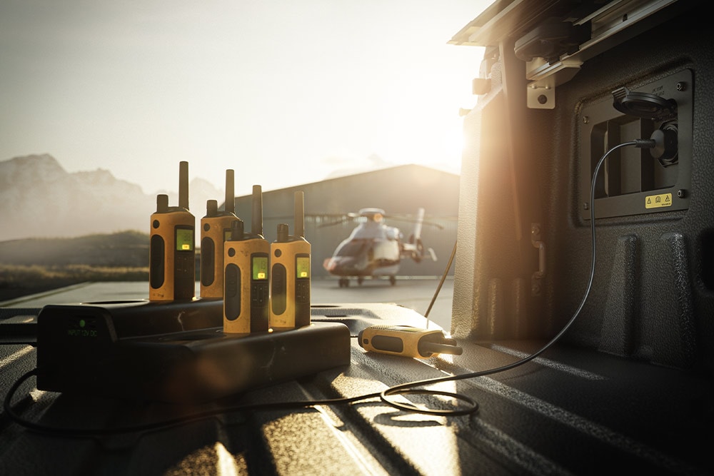 Vários walkie-talkies a carregar na plataforma de um Ranger Raptor ao pôr-do-sol, com um helicóptero ao longe.