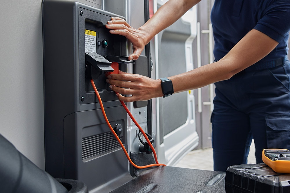 Grande plano de uma pessoa a ligar um cabo de carregamento no interior de um furgão elétrico Ford E-Transit.