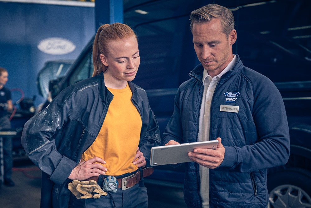 Dois mecânicos numa garagem a olharem para um tablet à frente de uma carrinha Ford E-Transit.