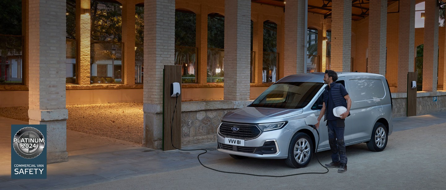 Um homem a segurar um capacete liga um cabo de carregamento de wallbox na nova Ford Transit Connect em Stardust Silver.