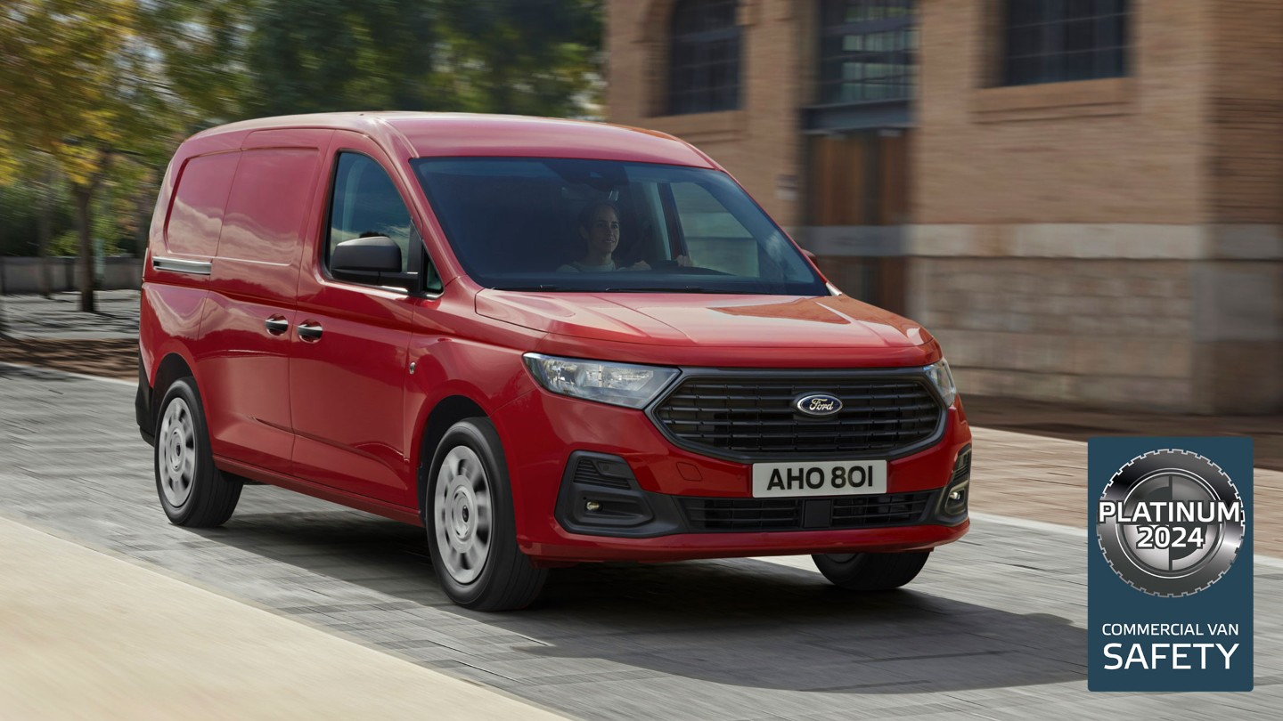 A nova Ford Transit Connect Trend em Maple Red desce uma estrada, mostrando a grelha dianteira e os faróis automáticos. 