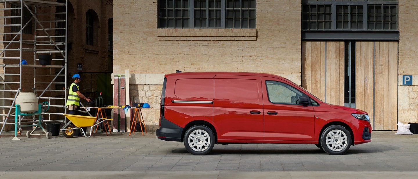 A nova Ford Transit Connect em Maple Red está estacionada no meio de um estaleiro de construção, mostrando a porta de carregamento lateral.