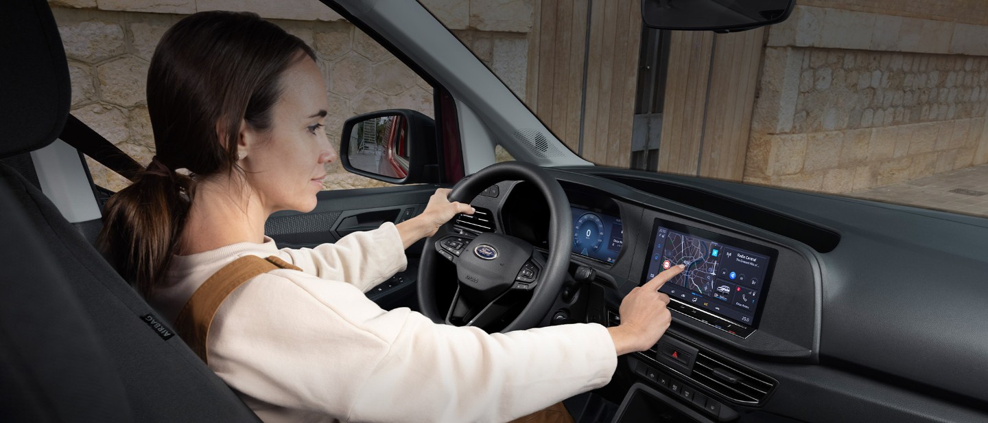 Uma mulher toca no ecrã tátil de 10" enquanto está sentada no banco do condutor da nova Ford Transit Connect.