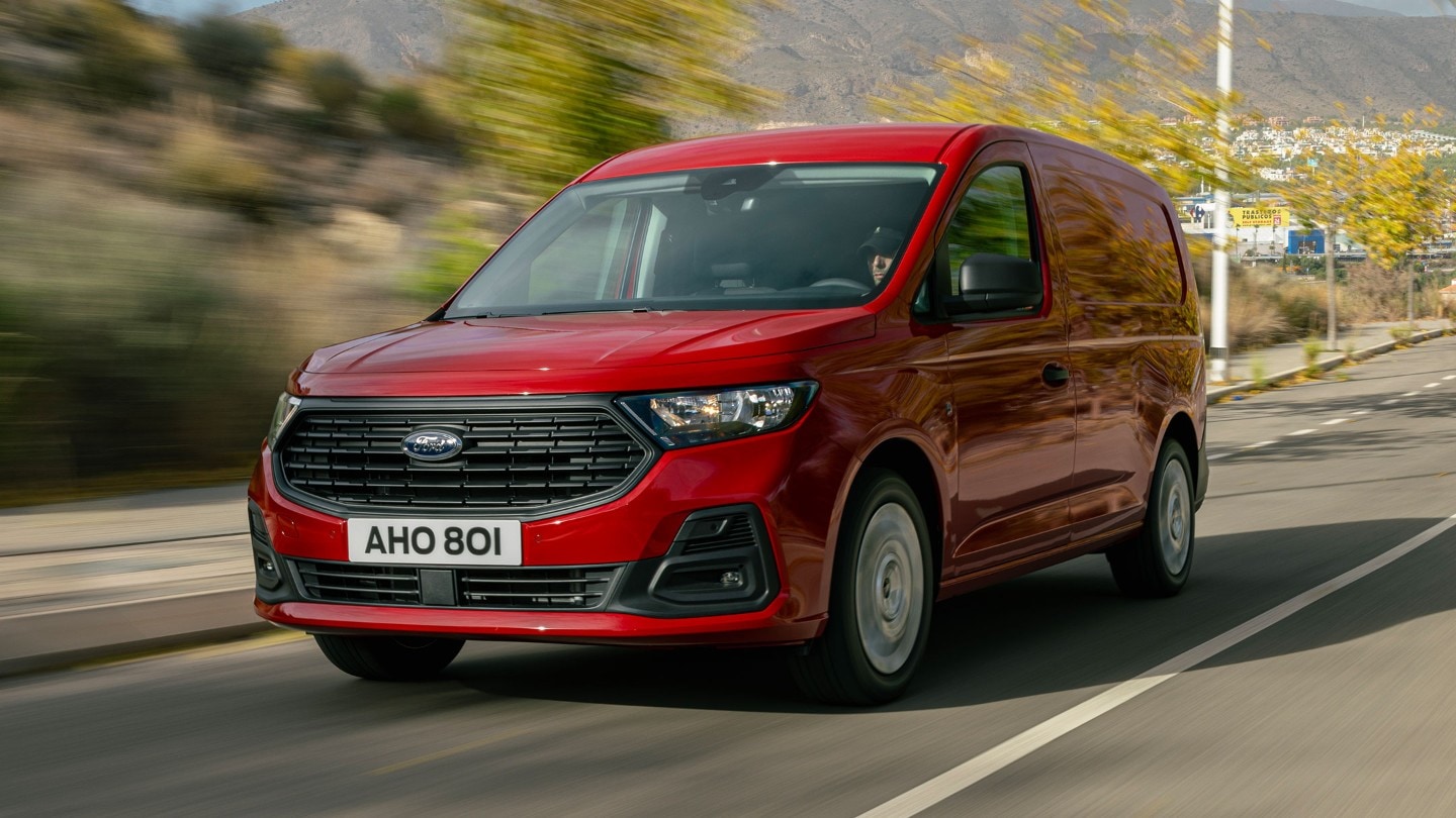 A nova Ford Transit Connect em Maple Red percorre uma estrada mostrando a grelha dianteira e os faróis.