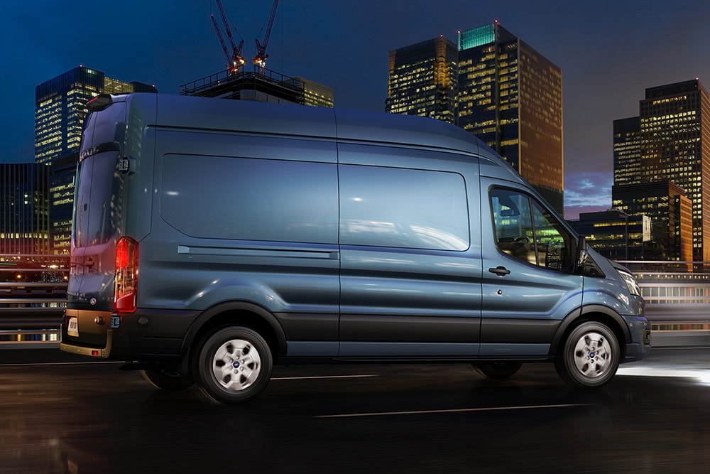 Ford Transit azul a circular numa rua urbana de noite. 